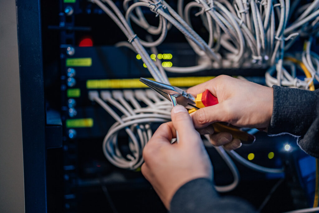 Hands of a technician working with wires and tool at data center.