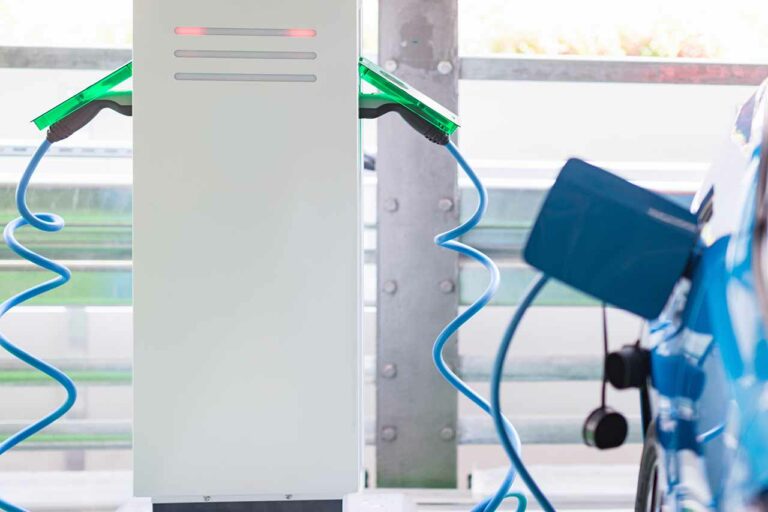 Electric vehicle (EV) charging station connected to a blue car in a modern industrial setting, showcasing advancements in EV infrastructure for 2025.