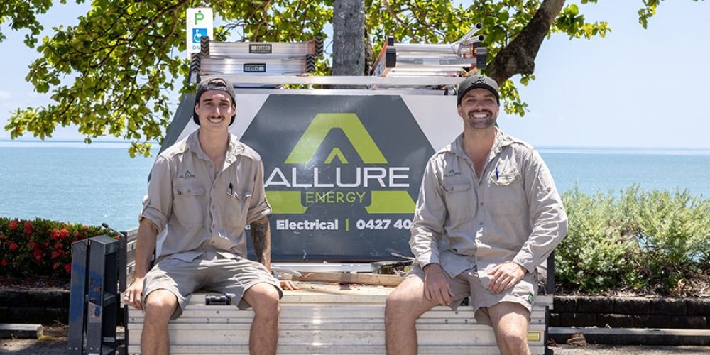 Allure Energy's friendly electricians in Cairns sitting on a work truck with the company's logo, ready for service.