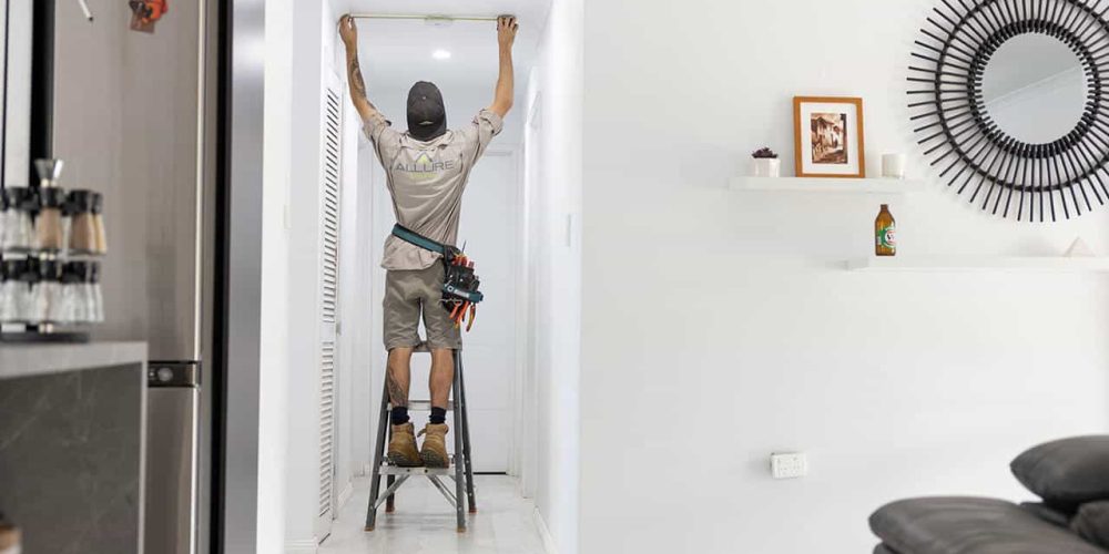 Allure Energy electrician measuring wall for smoke alarm installation in a Cairns home